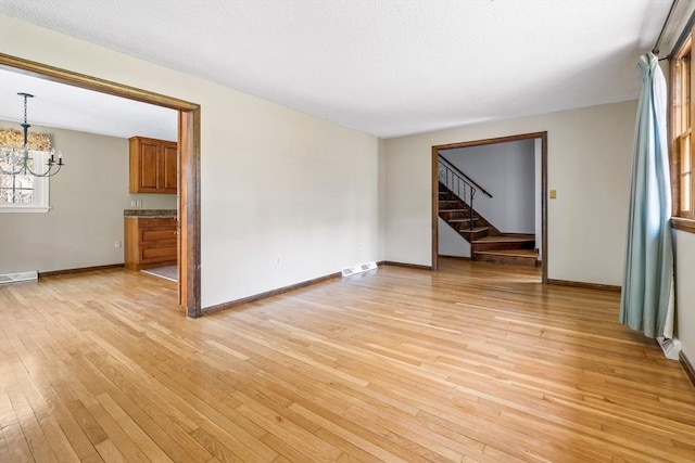 unfurnished living room featuring stairway, baseboards, light wood finished floors, and a chandelier