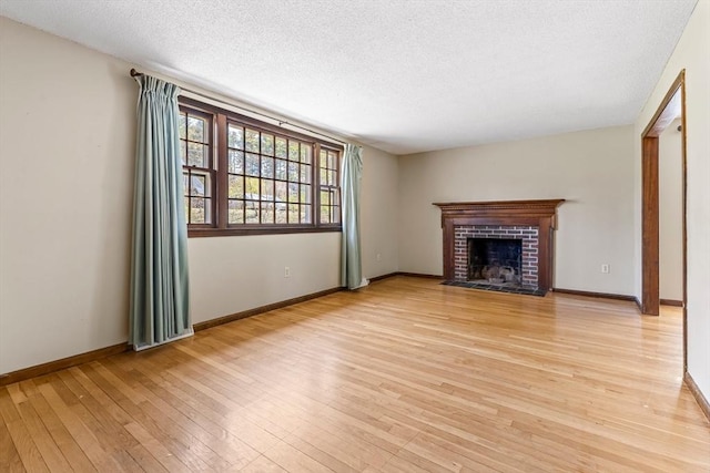 unfurnished living room with a fireplace, a textured ceiling, baseboards, and light wood-type flooring