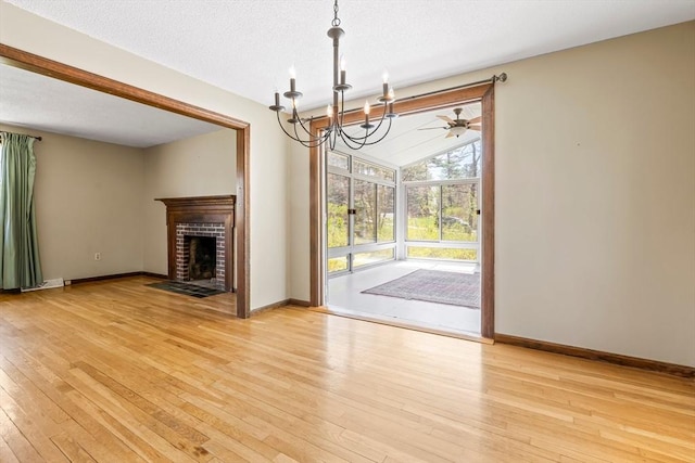 unfurnished living room featuring light wood-type flooring, baseboards, a brick fireplace, and a chandelier