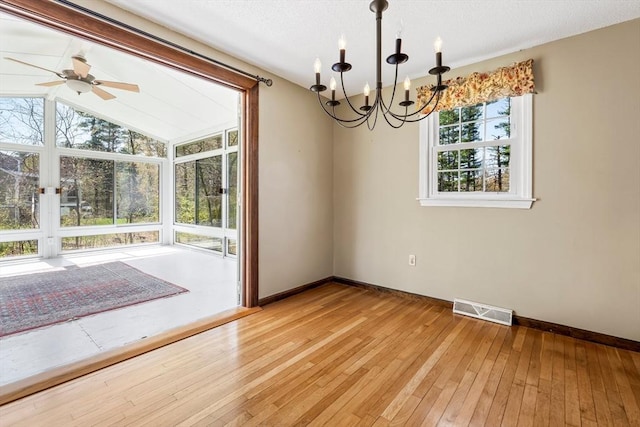 unfurnished dining area featuring visible vents, light wood-type flooring, baseboards, ceiling fan with notable chandelier, and lofted ceiling