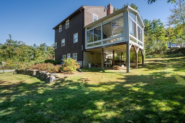 rear view of property featuring a sunroom, a yard, and a chimney