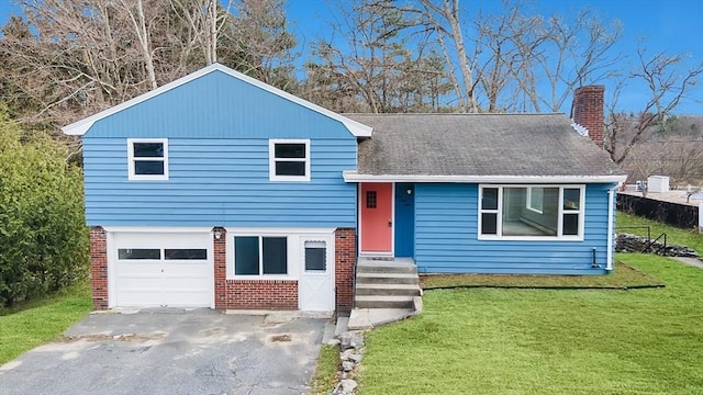 split level home with brick siding, a chimney, a front yard, and aphalt driveway