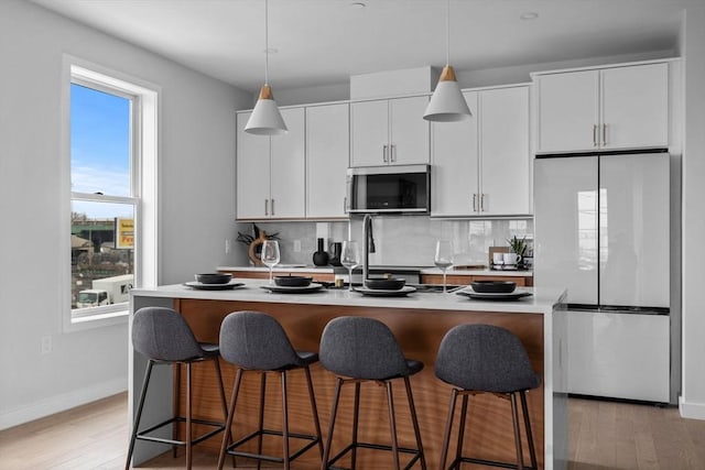 kitchen with light wood finished floors, appliances with stainless steel finishes, an island with sink, and backsplash