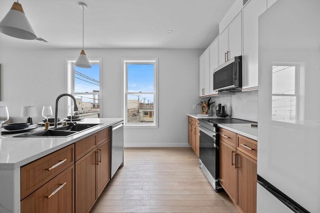 kitchen with a sink, white cabinets, appliances with stainless steel finishes, light wood-type flooring, and pendant lighting