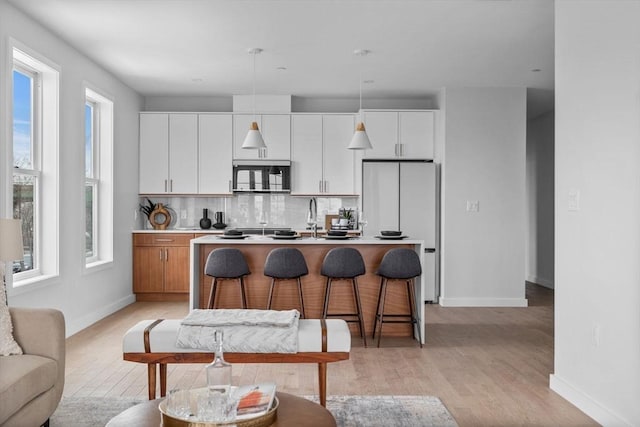 kitchen with light wood-style flooring, backsplash, freestanding refrigerator, stainless steel microwave, and an island with sink