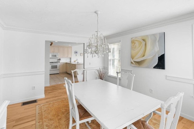 dining area with crown molding, visible vents, light wood-style floors, a chandelier, and baseboards