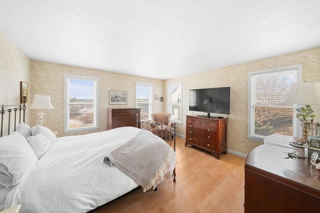 bedroom with baseboards, light wood finished floors, and wallpapered walls