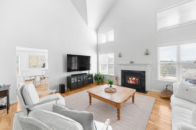 living area with light wood-style floors, baseboards, high vaulted ceiling, and a fireplace with flush hearth