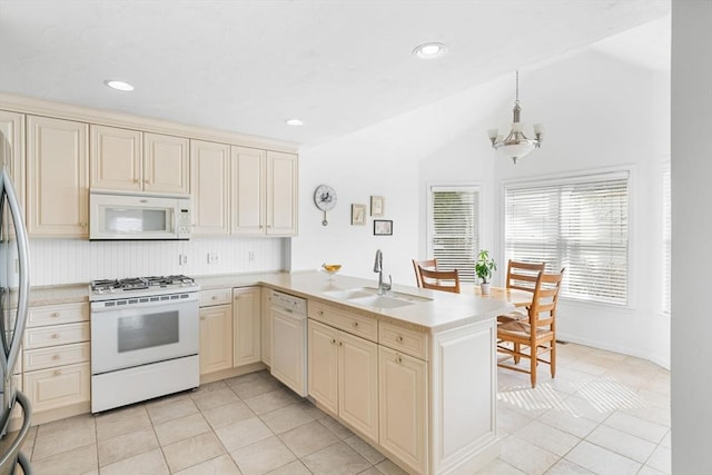 kitchen with light countertops, cream cabinets, a sink, white appliances, and a peninsula