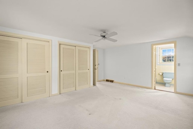 unfurnished bedroom featuring visible vents, baseboards, multiple closets, carpet, and ensuite bath