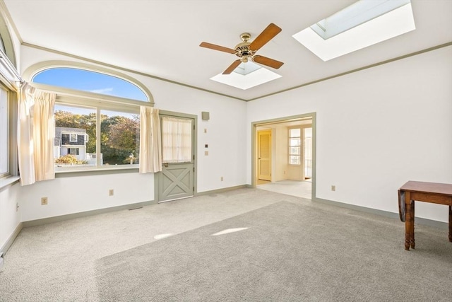 carpeted spare room featuring a healthy amount of sunlight, a skylight, baseboards, and crown molding