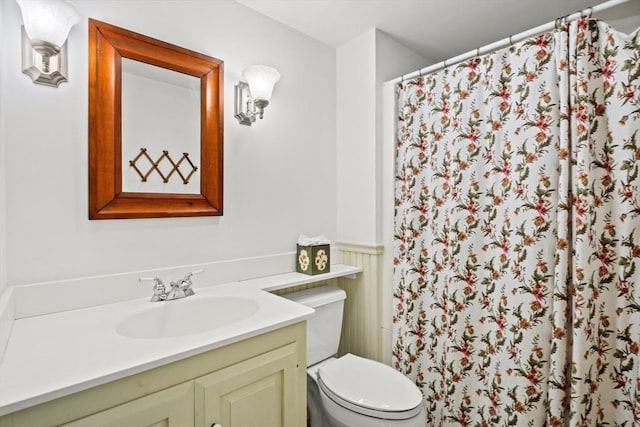 bathroom featuring curtained shower, a wainscoted wall, vanity, and toilet