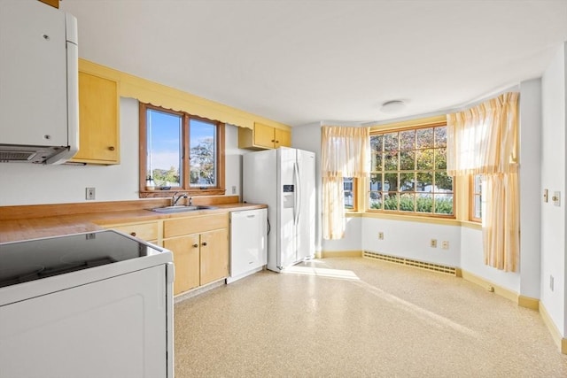 kitchen with white appliances, baseboard heating, light countertops, light brown cabinets, and a sink