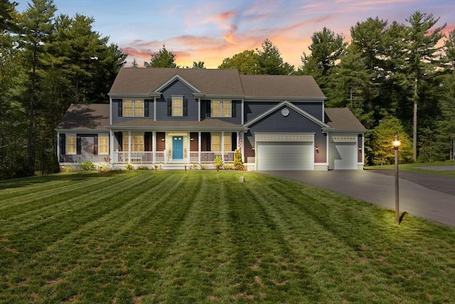 colonial house with driveway, covered porch, an attached garage, and a yard
