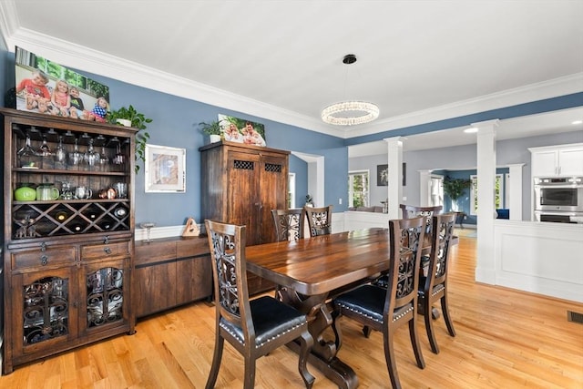 dining room with ornate columns, light wood finished floors, and ornamental molding