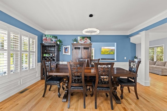 dining room featuring light wood-style floors, a wainscoted wall, crown molding, and decorative columns