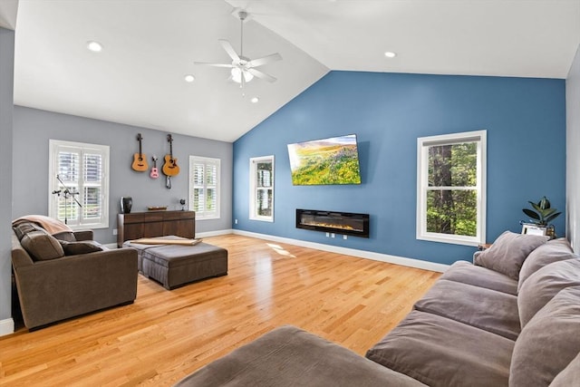 living room with ceiling fan, healthy amount of natural light, wood finished floors, a glass covered fireplace, and high vaulted ceiling