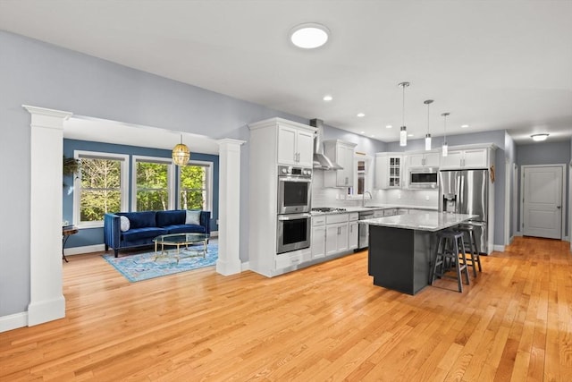 kitchen with stainless steel appliances, a sink, wall chimney range hood, white cabinetry, and a breakfast bar