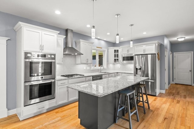 kitchen featuring stainless steel appliances, wall chimney exhaust hood, a sink, backsplash, and white cabinets