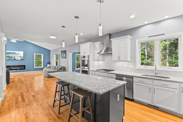 kitchen with appliances with stainless steel finishes, wall chimney range hood, a sink, a kitchen island, and decorative backsplash