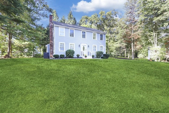 colonial house featuring a chimney and a front yard