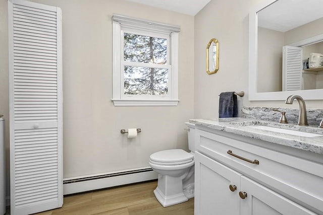 bathroom with toilet, a baseboard radiator, wood finished floors, vanity, and a closet