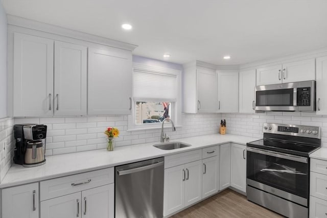 kitchen featuring light wood-style flooring, a sink, white cabinets, appliances with stainless steel finishes, and backsplash