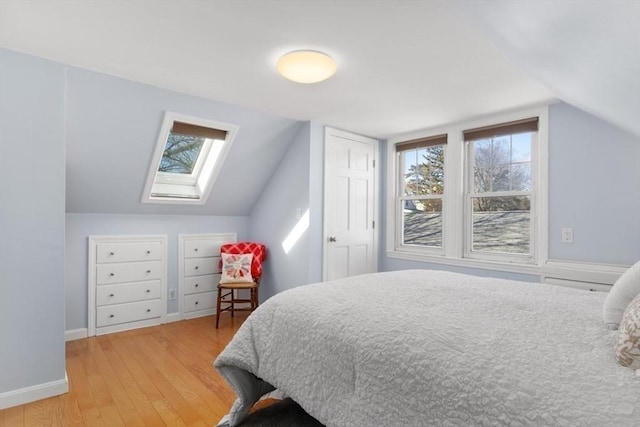 bedroom with lofted ceiling with skylight, light wood-type flooring, and baseboards