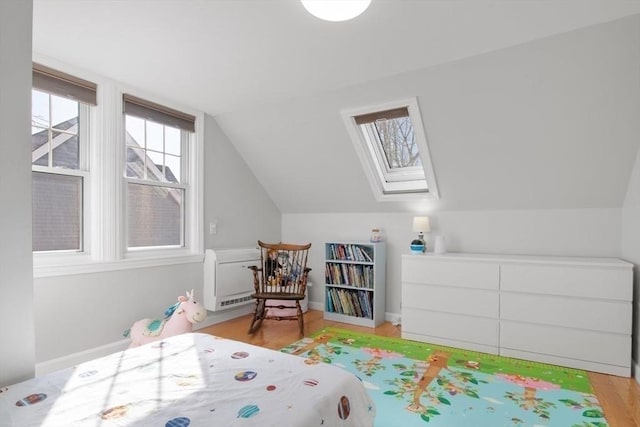 bedroom featuring light wood-style floors, vaulted ceiling with skylight, and baseboards