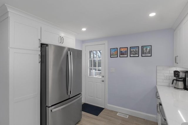 kitchen with baseboards, white cabinets, light wood-type flooring, backsplash, and freestanding refrigerator