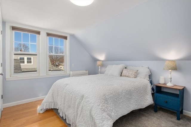 bedroom with vaulted ceiling, light wood-style flooring, and baseboards