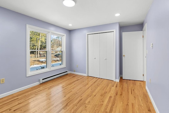 unfurnished bedroom with light wood-type flooring, a closet, and a baseboard heating unit