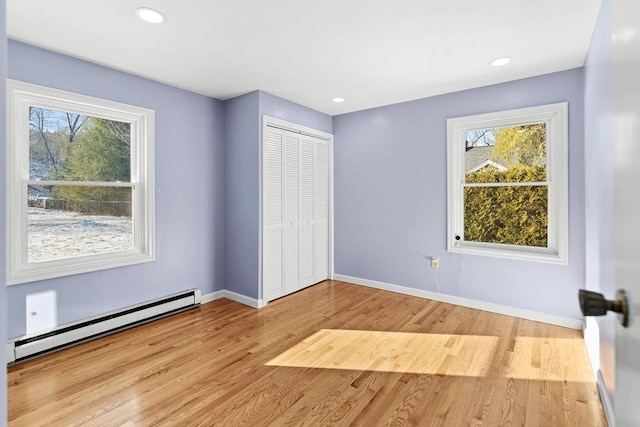 unfurnished bedroom with a closet, light hardwood / wood-style floors, multiple windows, and a baseboard radiator