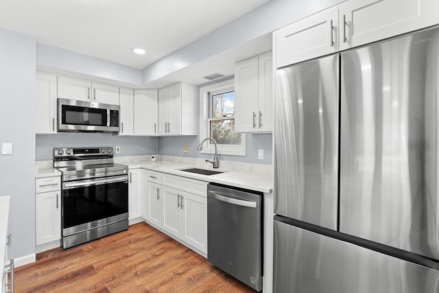 kitchen featuring white cabinets, appliances with stainless steel finishes, wood-type flooring, and sink