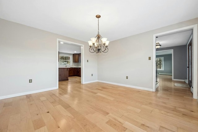 empty room with an inviting chandelier, light hardwood / wood-style flooring, and a baseboard heating unit