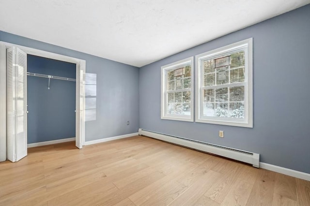 unfurnished bedroom featuring a baseboard heating unit, a closet, and light wood-type flooring