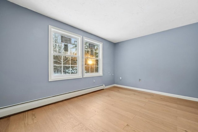 spare room featuring a baseboard heating unit and light wood-type flooring