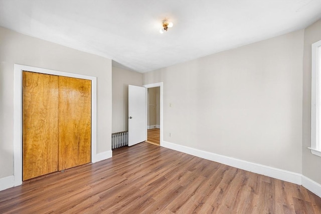 unfurnished bedroom with wood finished floors, baseboards, and radiator heating unit