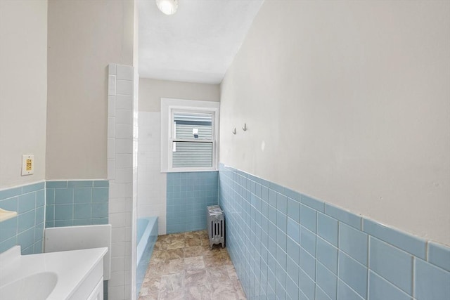 bathroom with radiator, tile walls, wainscoting, a bathtub, and vanity