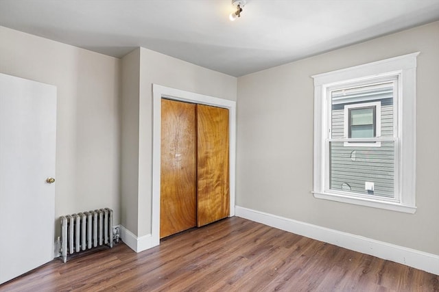 unfurnished bedroom featuring radiator, baseboards, wood finished floors, and a closet