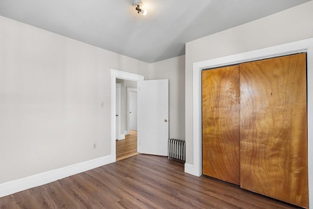 unfurnished bedroom featuring wood finished floors, baseboards, and a closet