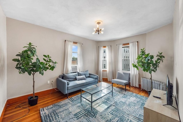 living room with radiator, baseboards, wood finished floors, and a chandelier