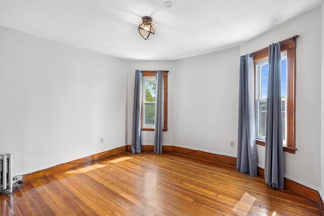 unfurnished room featuring wood-type flooring, baseboards, and radiator
