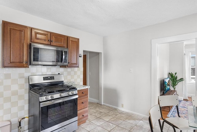 kitchen with appliances with stainless steel finishes, brown cabinets, baseboards, light tile patterned floors, and tasteful backsplash