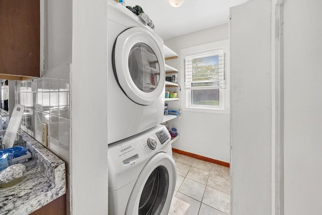 clothes washing area with stacked washer / dryer, baseboards, and light tile patterned floors