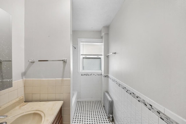 bathroom featuring tile walls, radiator heating unit, wainscoting, and vanity