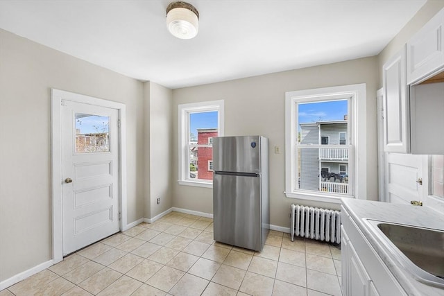 kitchen with radiator heating unit, freestanding refrigerator, a sink, and white cabinetry