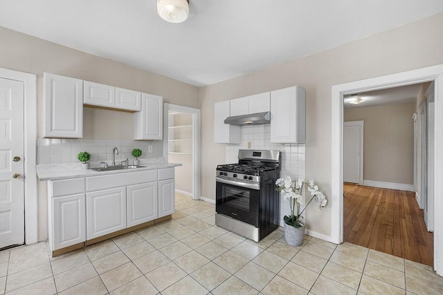 kitchen with gas range, under cabinet range hood, a sink, light countertops, and backsplash