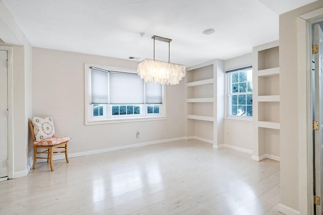 unfurnished dining area featuring light wood-type flooring, built in features, and a chandelier