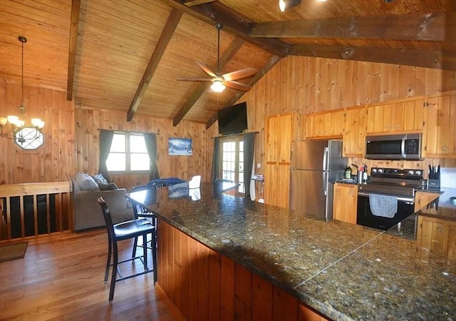 kitchen featuring wooden walls, wood-type flooring, beamed ceiling, stainless steel appliances, and a healthy amount of sunlight